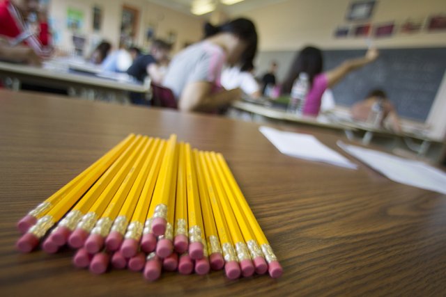 Un tas de crayons à papier avec gomme posés sur une table de classe, des élèves en fond. Lieu où apprendre.
