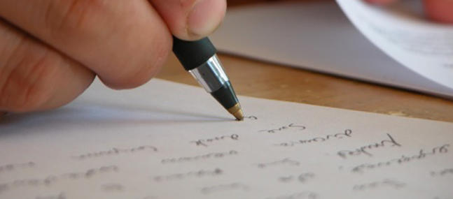 Une personne écrit au bic sur un papier