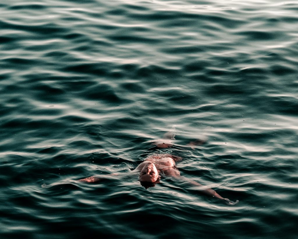 Un homme flotte à la surface d'une étendue d'eau extérieure, se laissant porter par le courant
