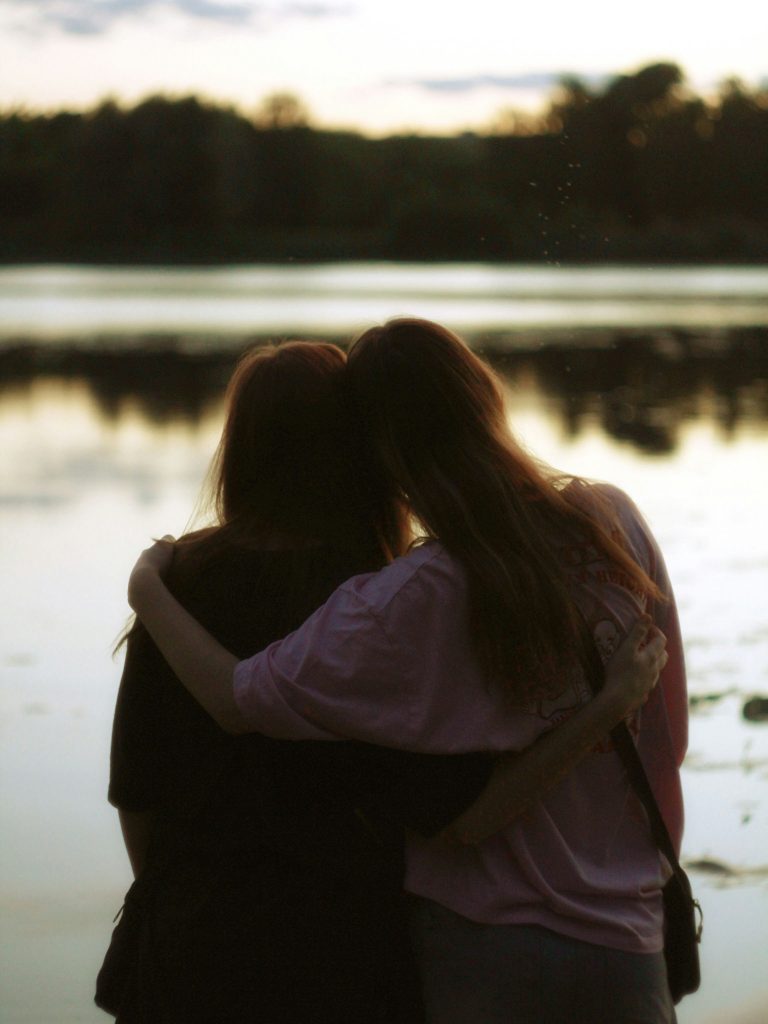 Deux femmes enlacées devant une étendue d'eau au crépuscule, soutien moral
